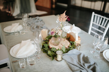 Vintage wedding decor. Beautiful event venue. Creative decoration. Hall decoration. Festive table decor. Stylish stone tablet with table number in grey, green branches and peonies, candles in gold can