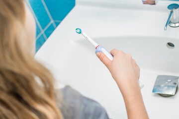 Electric oscillating toothbrush in woman hand in bathroom at home. Sholder view. Prevention of teeth decay, white and healthy teeth concept.