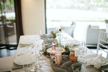 Vintage wedding decor. Beautiful event venue. Creative decoration. Hall decoration. Festive table decor. Stylish stone tablet with table number in grey, green branches and peonies, candles in gold can