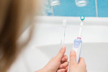 Electric oscillating  and manual toothbrush in woman hand in bathroom at home. Sholder view....