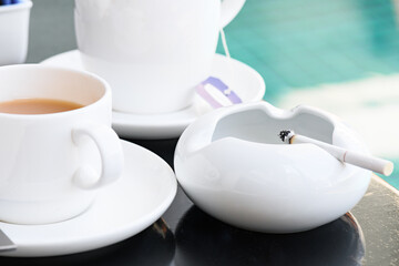Cigarettes are placed in a white ceramic ashtray beside a coffee mug.