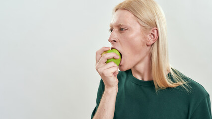 Handsome young caucasian guy biting green juicy apple