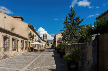 Nice image of the empty streets of a typical medieval town with the church tower in the background and a blue sky with white clouds