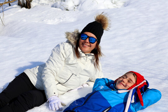 Madre he hijo tumbados en la nieve sonriendo y felices.