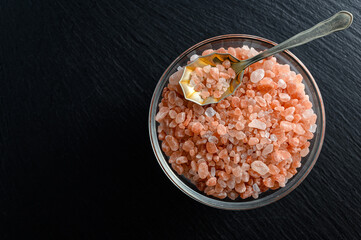 Glass bowl of himalayan salt and small spoon on black background