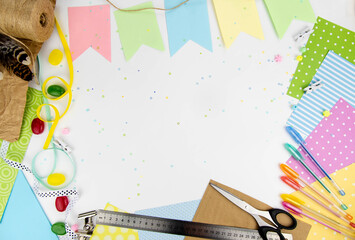 Spring background with free space. View from above on the white background with an ornament of multi-colored paper, ribbons, colored pens, scissors, ruler.