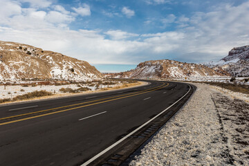 Wide empty highway splitting snow covered hills in rural New Mexico on cloudy day