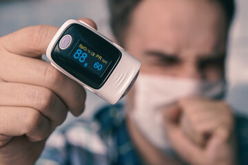 oxygen saturation of the blood. pulse oximeter on a mans finger. A patient in a medical mask...