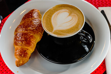 Cappuccino in a cup with croissant in table