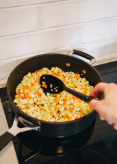 Vegetable preparation, stirring carrot, onion and celery in frying pan with spoon