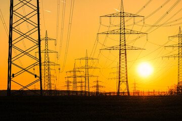 Electricity poles and electric power transmission lines against vibrant orange sky at sunset on a...
