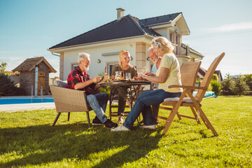 Elderly friends having an outdoor lunch in the backyard by the swimming pool