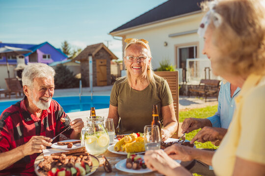 Senior friends eating lunch by the swimming pool - Powered by Adobe