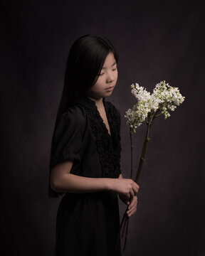 classic painterly studio portrait of a girl in black dress with a branch of white lilac spring flowers