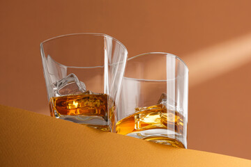 modern still life in warm colors. two glasses with whiskey with ice on the edge of the surface in the rays of light.