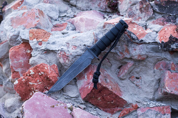 Large black knife on a background of red bricks. Knife with a lanyard.