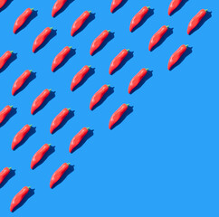 Trendy pattern made  of red chilli peppers on pastel blue background with diagonal copy space. Hot food concept.