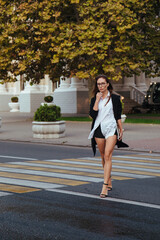 A girl rushes to a business meeting, crossing a big city street at a pedestrian crossing.