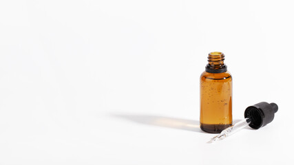 cosmetic oil in glass bottle with pipette, white background, hard light and shadows