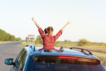 Travelling by car. The girl looks out of the car hatch.  young woman sitting  on the car roof  and...