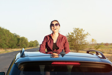 Travelling by car. The girl looks out of the car hatch.  young woman sitting  on the car roof  and...