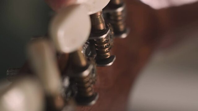 man is tuning musical instrument. The musician twists the guitar tuner pegs and pulls the strings to start playing music. Extreme close up footage.