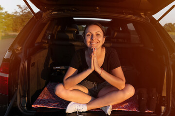 Plakat happy beautiful girl sitting in the trunk of car and enjoying sunset on the roadside. young woman in the car