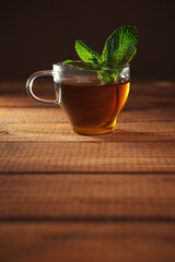 Glass cup of herbal tea with fresh mint on wooden table with brown background. Vertical shot with copy space.