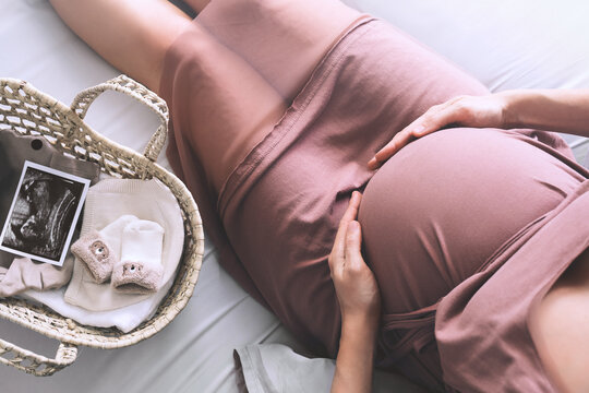 Pregnant woman in dress holds hands on belly. Expectant mother waiting and preparing for baby birth during pregnancy.
