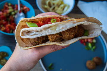 Hand showing fresh gluten free tortilla wrap stuffed with chickpea falafel, fresh vegetables chopped salad, fried onion rings, jalapenos, mayo and scallions. Healthy tasty meal preparation. Top view.
