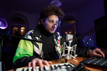 Young composer making a music with modern musical equipment a Midi keyboard a Drum pad and a Microphone in dark room.