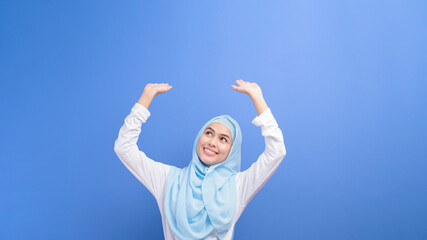 Portrait of a young muslim woman with hijab over blue background studio.