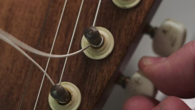 man is tuning musical instrument. The musician twists the guitar tuner pegs and pulls the strings to start playing music. Extreme close up footage.