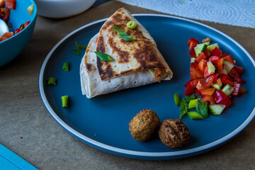 Fresh gluten free tortilla wrap burned on a pan stuffed with chickpea falafel, fresh vegetables chopped salad, fried onion rings, jalapenos, mayo and scallions. Tasty meal preparation. Side view.