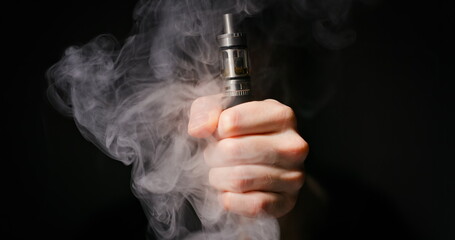 Electronic cigarette grabbed by male hand against dark background and vapor