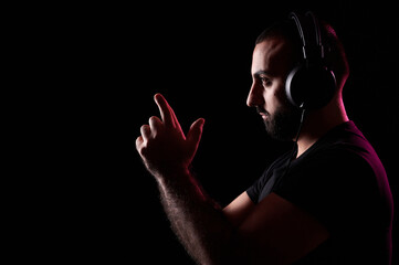 Bearded young Arab DJ musician listens music with headphones and depicts gun with his hands. International DJ Day