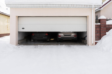 xterior of a garage attached to a house. garage with two cars inside in winter. semi-open sectional doors