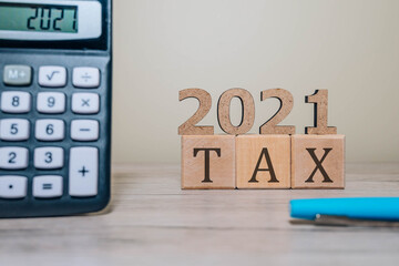 TAX 2021 on wooden cubes, calculator and a pen on a wooden table. Tax 2021 - phrase from wooden...