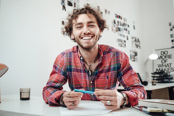 Happy man in shirt with a pencil poses in comfortable office sitting at table and looking at camera. - obrazy, fototapety, plakaty