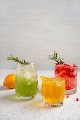Fototapeta premium Three colorful summer cocktails in glasses on white table. Assortment of fresh summer drinks. Red sangria cocktails, orange punch cocktail, margarita cocktail, tropical mule.