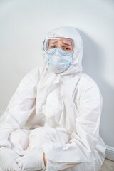 Fototapeta na wymiar portrait of a tired woman doctor in a protective suit, glasses, mask and glove against the white wall. the hard, dangerous and responsible work of medics during the pandemic. coronavirus in the world.