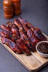 Fried chicken wings on a wooden board with barbecue sauce. Black background, close-up.