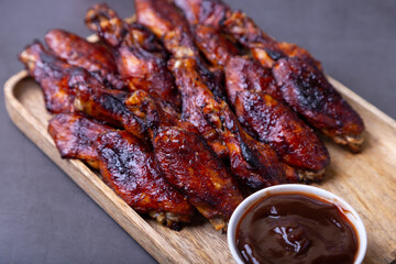 Fried chicken wings on a wooden board with barbecue sauce. Black background, close-up.