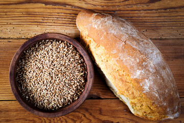 wheat grains in ceramic bowl and bread on wooden table