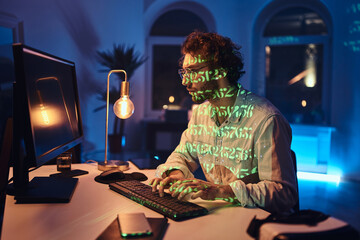 Portrait of a caucasian freelancer with glasses doing his work using desk computer in dark office room with lights.
