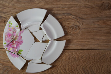 Shards of a broken plate on the wooden floor. Broken white ceramic plate on the wooden floor....