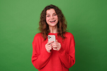 Beautiful young girl in red clothes on a green background. The girl laughs at the camera from the received message. The concept of emotions