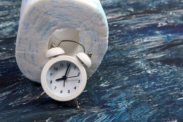 alarm clock and toilet paper. Concept of constipation, indigestion, digestion problem