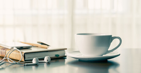 Coffee cup on note book with smart phone and headphones on desk in holiday, concept of study online