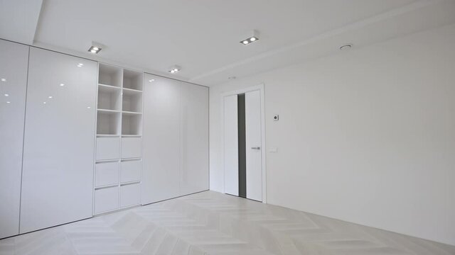 Vacant unfurnished room interior with wooden herringbone parquet floor and white walls and ceiling lit by down lights.